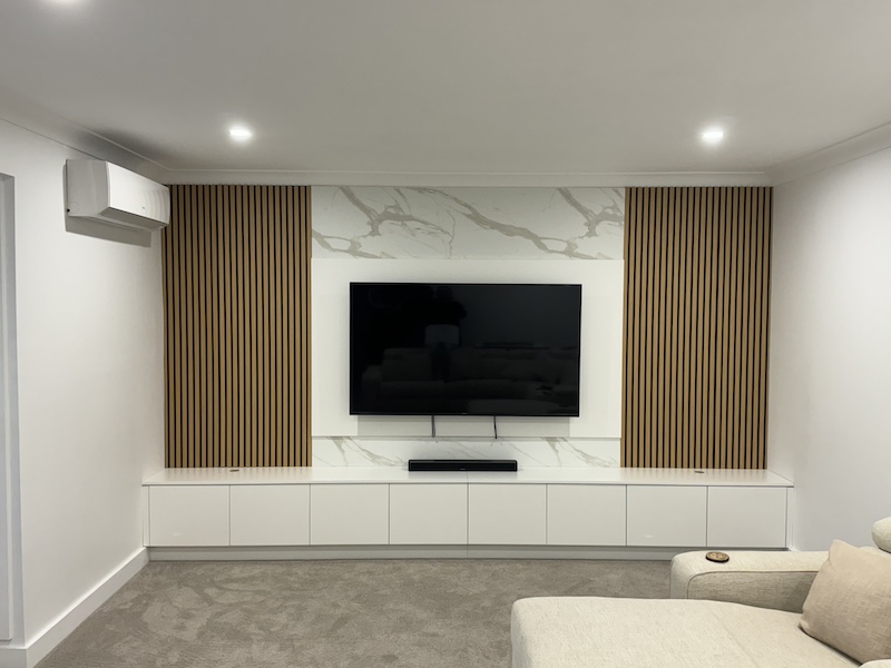 Discover the elegance of a modern home theatre setup by Dura Group, a leading Sydney-based family-owned building company specializing in customized renovations. This stylish design features a state-of-the-art television mounted against a sophisticated backdrop of marble and wooden panels, offering a perfect blend of aesthetics and functionality. Dura Group, led by Managing Director Mark with over 27 years of experience, excels in creating personalized home environments across the Sutherland Shire, Bayside, Inner West, Georges River, and Randwick regions. Our expertise in home renovations, ground floor extensions, upper storey additions, kitchen upgrades, bathroom remodels, and laundry renovations ensures top-notch outcomes tailored to your needs. Prioritizing time efficiency, budget-conscious planning, and transparent communication, Dura Group guarantees home improvement ideas without compromising on build quality. Transform your living room into a high-end entertainment hub and enjoy an exceptional viewing experience at home. Contact us today for a consultation, and let&rsquo;s bring your dream home vision to life with Dura Group&rsquo;s homeowner-first focus on trust and transparency.